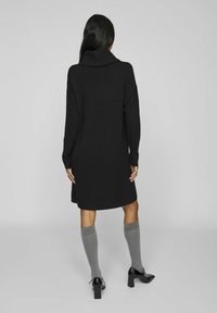 Black knitted dress with a high collar, long sleeves, and ribbed cuffs, paired with gray knee-high socks and black heeled shoes.