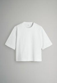 Balta apkirpta trumpa rankovė T-shirt su apvalia apykakle, pateikta neutralioje pilkoje fone.