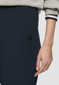 Navy blauwe joggingbroek gemaakt van zachte stof, met een klein zwart hart borduurdetail aan de zijkant en een ontwerp met elastische tailleband.