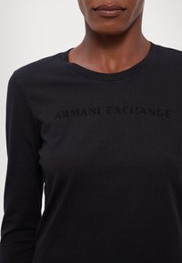 Maglietta nera a maniche lunghe realizzata in un morbido tessuto, con la scritta "ARMANI EXCHANGE" in un design tonale sottile sul petto.