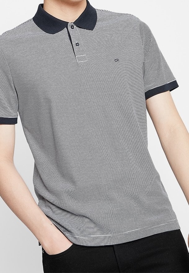Homme portant un polo à manches courtes rayé gris et blanc avec col et poignets noirs, une main dans la poche du pantalon noir.