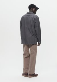 Gray long-sleeve shirt with vertical stripes, brown corduroy pants, and brown shoes with laces, viewed from the back. Black cap worn.