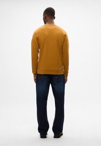 Felpa gialla senape con colletto a girocollo, polsini e orlo a coste. Abbinata a un paio di jeans in denim blu scuro e sandali neri.