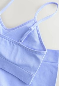 Lyse lilla bomulds camisole med justerbare stropper og en glat tekstur, har en ribbet kant forneden og et sømløst design.
