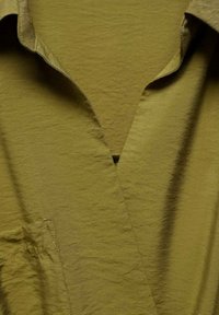 Olive green shirt with a slightly crinkled texture, V-neck collar, and left chest pocket. The fabric is soft and lightweight.