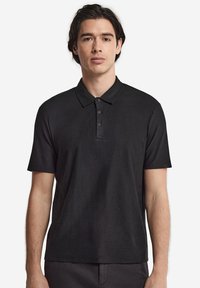 Svart polo-shirt med krage, korta ärmar och treknapprad. Tillverkad av mjukt tyg med en subtil textur.