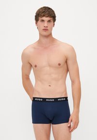 Navyblaue Boxer-Shorts mit einem schwarzen Bund, der das weiße Logo "HUGO" trägt. Glattes Material, eng anliegendes Design und Oberschenkellänge.