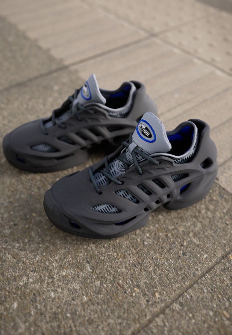 Zapatillas deportivas grises con paneles de malla, superposiciones texturizadas y un collar acolchado. Presenta un logo azul y cortes para la transpirabilidad.