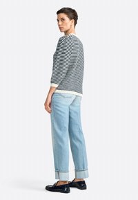 Striped sweater in navy and cream, three-quarter sleeves. Paired with light blue cuffed jeans and black loafers. Minimalist design.