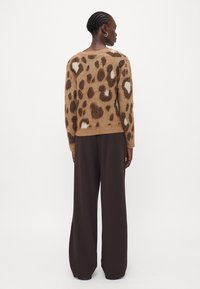 Brun leopardmønstret genser laget av mykt materiale, med lange ermer, ribbestrikket kant og avslappet passform, sammen med vide svarte bukser.