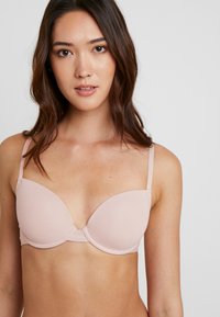 Soutien-gorge rose clair avec des coupes lisses et rembourrées, des bretelles réglables et un détail de couture centrale pour le soutien. Conçu pour le confort et un port quotidien.