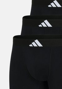 Svarta sportshorts med svart elastiskt midjeband som har tre vita diagonala ränder. Slät tygtextur och figurnära design.