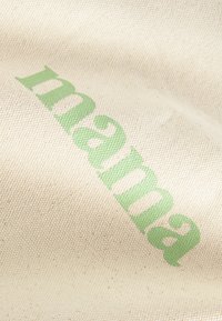 Naturlig canvas tyg med ordet "mama" i fet grön text, som betonar struktur och enkel design.
