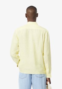 Camicia a maniche lunghe a righe gialle e bianche, con colletto classico e polsini con bottone, realizzata in tessuto leggero con una vestibilità rilassata.