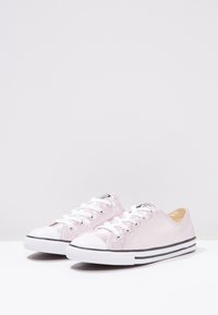 Světle růžové plátěné tenisky s bílým gumovým špičkou a černým proužkovaným skořepinou. Mají šněrovací design a texturovaný svršek.