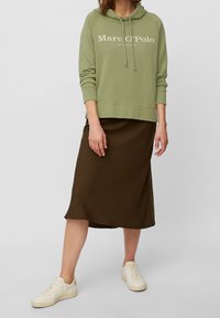 Lichtgroene hoodie met witte logo, gecombineerd met een bruine satijnen midi-rok en witte sneakers. Heeft een relaxte pasvorm en een verstelbare trekkoordkap.