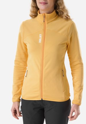 Person wearing a yellow zip-up fleece jacket with two zippered pockets and "MILLET" logo on the chest, paired with black pants.