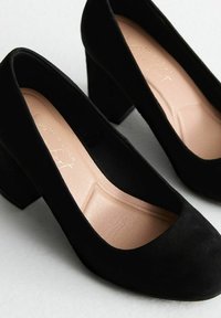 Scarpe alte nere in camoscio con punta arrotondata, tacco a blocco moderato e una soletta interna beige liscia. Design semplice, senza decorazioni visibili.