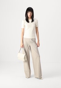 Beige geribbelde top met korte mouwen gecombineerd met een beige broek met wijde pijpen. Houdt een crèmekleurige handtas vast met een zilveren schouderriem. Textuurdetails van de stof zichtbaar.