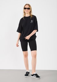 T-shirt oversized preto com um gráfico de flor branca, combinado com calções de ciclismo ribados pretos e sapatos pretos com riscas brancas.