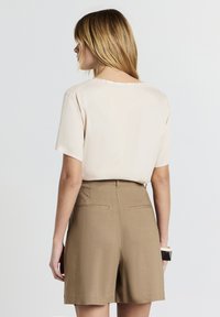 Blusa beige a maniche corte con collo rotondo, abbinata a pantaloni shorts beige chiaro, dotati di tasche posteriori e una texture liscia.