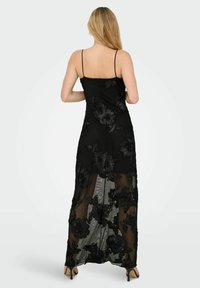 Juoda maxi suknelė su plonomis petnešėlėmis, puošta sudėtinga siuvinėjimu ir permatomu audiniu. Suknelės ilgis siekia kulkšnis, leidžiantis matyti avalynę.