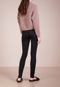 Luddig, pastellrosa tröja med rund hals, matchad med svarta skinny jeans och svarta luddiga tofflor, sedd bakifrån.