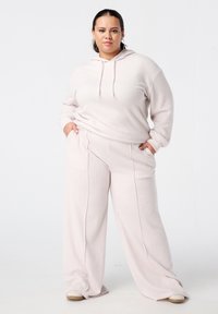 Lichtroze geribde hoodie met trekkoorden, gecombineerd met bijpassende wijde broek met zijzakken en contrasterende verticale naden.