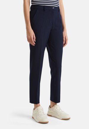 Pantalons habillés navy en tissu lisse, avec un design ajusté, des poches latérales et une fermeture à bouton. Assortis à des baskets blanches.