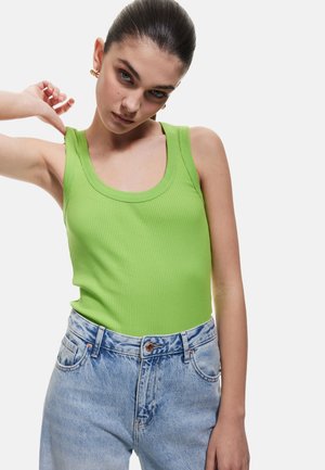 Top de tirantes verdes acanalados con tirantes anchos y escote en forma de scoop, combinado con jeans de mezclilla de tiro alto en un tono azul claro con una textura lavado.