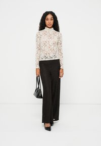 Top in pizzo a maniche lunghe color avorio con motivo floreale, abbinato a pantaloni neri a gamba larga con vita alta. Accessoriato con una piccola borsa nera.