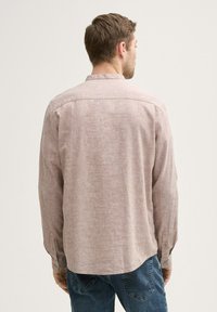 Camisa de manga larga de color marrón claro, hecha de tela texturizada. Cuenta con un cuello abotonado, puños abotonados y un dobladillo curvo.