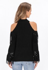 Czarny sweter typu cold-shoulder z frędzlami i cekinowymi detalami na rękawach. Wykonany z miękkiego materiału, z wysokim kołnierzem i luźnym krojem.