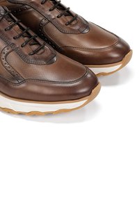 Zapatillas de cuero marrón con una parte superior texturizada, acentos perforados, cordones negros y una suela contrastante en blanco y color goma.