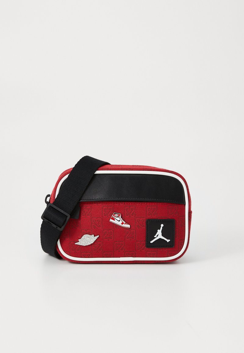 Rote Crossbody-Tasche aus Stoff mit schwarzen Akzenten, verstellbarem Tragegurt und Patches, darunter ein Turnschuh und das Jordan-Logo. Mit Reißverschlussverschluss.