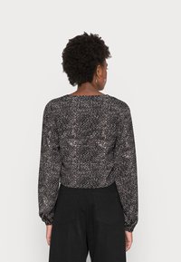 Blusa preta com padrão manchado em branco, mangas longas, decote redondo e punhos franzidos, combinada com calças pretas de cintura alta.