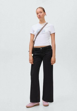 Jeans neri a gamba larga con vita alta, abbinati a una maglietta cropped bianca con una grafica di motocicletta azzurro chiaro e sneakers rosa.