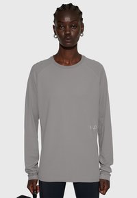 Långärmad, ljusgrå träningsöverdel med strukturerad design och raglanärmar. Har en liten "H.L.O"-logga på framsidans nedre vänstra del.