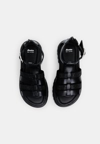 Czarne skórzane sandały z grubymi paskami, posiadające teksturowany, pleciony wzór oraz pasek na kostkę z klamrą. Wyposażone w wyściełaną wkładkę i gumową podeszwę.