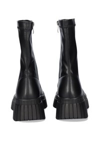 Botas negras de tobillo hechas de suave cuero sintético con una suela gruesa acanalada, que cuentan con un cierre lateral y un diseño ajustado.