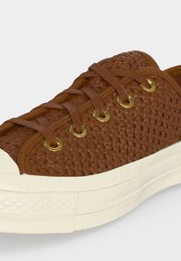 Basket en cuir tressé marron avec des lacets couleur cuir, des œillets dorés, un embout en caoutchouc blanc et une semelle blanche épaisse.