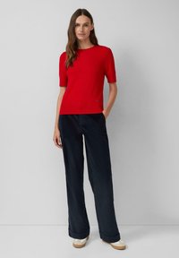 Czerwony top z krótkim rękawem w połączeniu z granatowymi spodniami o szerokich nogawkach. Ubranie charakteryzuje się gładką fakturą i subtelnym detalem logo na dole.