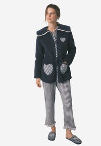 Accappatoio in felpa navy con ampio colletto e tasche a forma di cuore; abbinato a pantaloni a quadretti e ciabatte con orli arricciati e dettagli floreali.