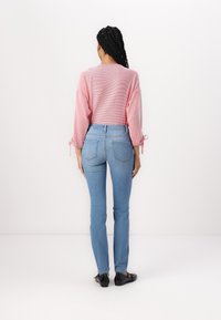 Top de manga larga a rayas rosa claro con detalles de lazo, combinado con unos jeans ajustados azul claro y zapatos planos negros. Bolsillos traseros visibles en los jeans.