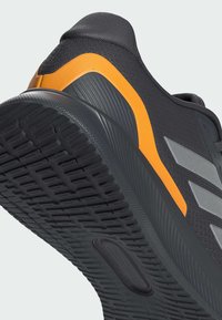 Schwarzer Sportschuh mit strukturiertem Obermaterial, orangefarbenem Akzent und gestreiftem grauem Logo. Die Gummisohle verfügt über ein gerilltes Muster für besseren Halt.