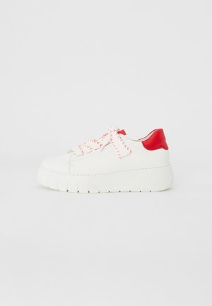 Sneaker blanc avec une épaisse semelle blanche et un talon rouge, présentant un matériau texturé, des lacets rouges vifs avec des rayures blanches, et un design minimaliste.