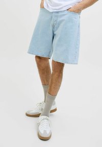 Pantalones cortos de mezclilla azul claro con un ajuste holgado, que cuentan con bolsillos laterales y un diseño clásico de cinco bolsillos. Combinados con zapatillas blancas y calcetines grises.