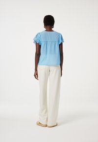 Lichtblauw blouse met oogjesafwerking op de korte mouwen, geplooide epi, gecombineerd met witte wijde broeken en naturel espadrille schoenen.