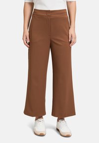 Pantaloni marroni a gamba larga realizzati con un tessuto morbido. Caratterizzati da una vita piatta e pieghe frontali. Abbinati a sneakers bianche per un contrasto.