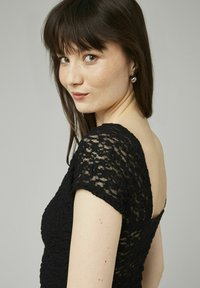 Robe en dentelle noire avec des manches courtes, tissu texturé et un décolleté profond dans le dos. Présente une silhouette ajustée et un subtil éclat.